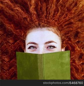 Young redhead woman covering by a book