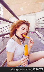 Young redhead woman eating an orange ice cream