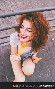 Young redhead woman enjoying an orange ice cream