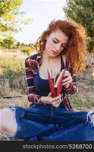 Young redhead woman reading a book outdoors