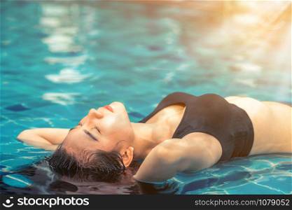 Young relaxed woman at swimming pool in summer in luxury beach resort. Travel and lifestyle.
