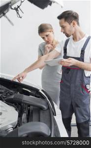 Young repair worker explaining car engine to worried customer in workshop