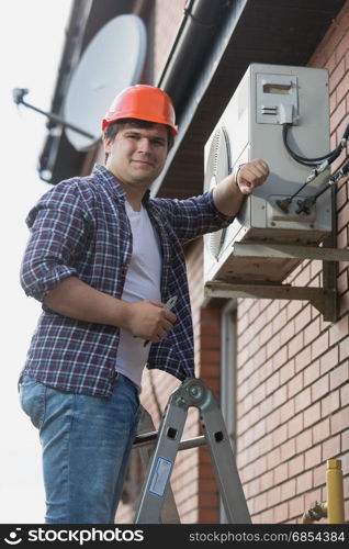 Young repairman installing air conditioner on outer wall
