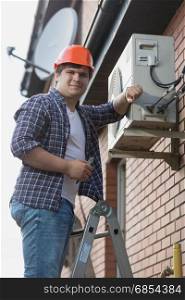 Young repairman installing air conditioner on outer wall