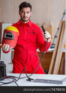 Young repairman with a welding gun electrode and a helmet welding metal. Young repairman with a welding gun electrode and a helmet weldin