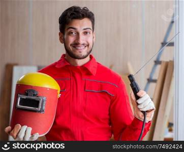 Young repairman with a welding gun electrode and a helmet welding metal. Young repairman with a welding gun electrode and a helmet weldin