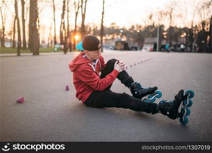Young roller skater sitting on asphalt in city park. Male rollerskater, extreme sport
