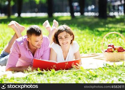 Young romantic couple lying in park and reading book. Having rest in park