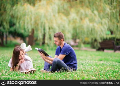 Young romantic couple lying in park and reading books. Relaxed young couple reading books while lying on grass