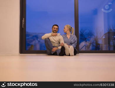 Young romantic couple sitting on the floor in front of fireplace,talking and drinking tea on cold winter night at home