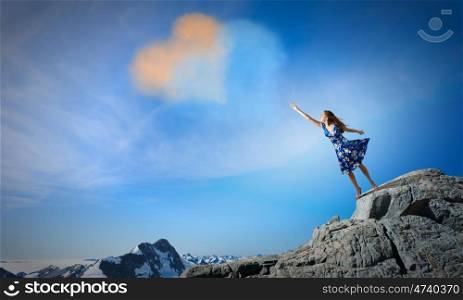 Young romantic woman in summer dress reaching love heart. Love and romance