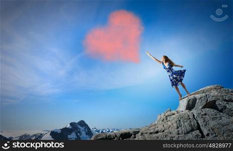 Young romantic woman in summer dress reaching love heart. Love and romance