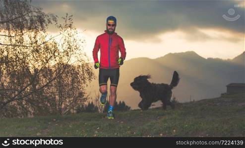 Young runner in the mountains with the dog beside him who follows him and wants to play