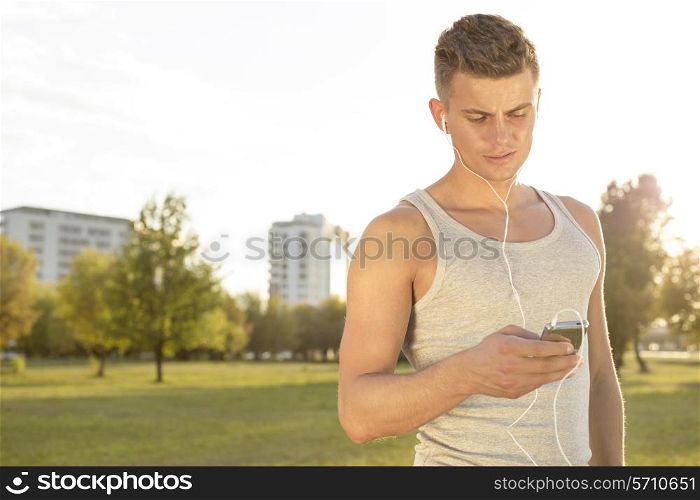 Young runner listening to music through cell phone in park