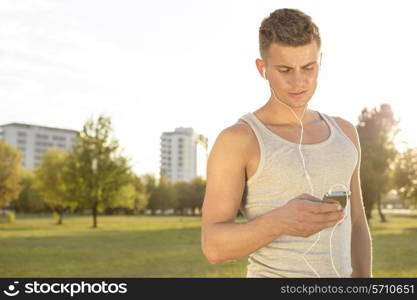 Young runner listening to music through cell phone in park