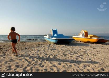 young running boy and a beach with two yellow and blue pedalos