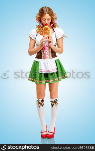 Young sad sexy Oktoberfest woman wearing a traditional Bavarian dress dirndl holding a pretzel in hands on blue background.