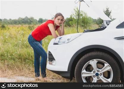 Young sad woman leaning on broen car at countryside