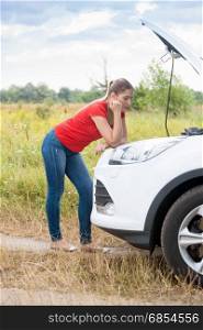 Young sad woman looking at broken car and waiting for help