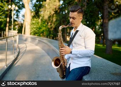 Young saxophonist plays the saxophone in summer park. Musician with sax outdoors, musical performance in nature, jazz performer. Young saxophonist plays the saxophone in park