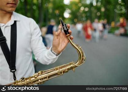 Young saxophonist with saxophone on the alley in summer park. Musician with sax outdoors, musical performance in nature, jazz melody performer. Young saxophonist with saxophone on alley in park