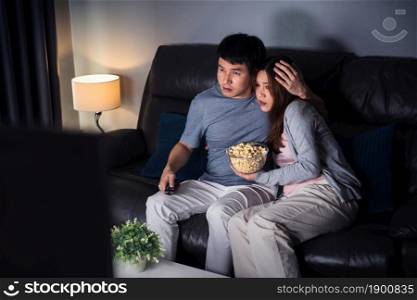 young scared couple is watching horror movie TV on sofa at night