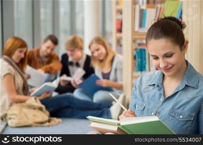Young school student studying with friends in background at library