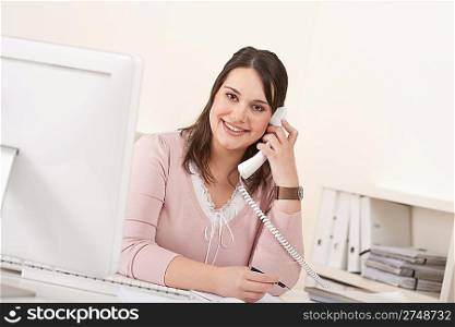 Young secretary on phone at modern office in front of computer