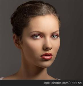 young sensual lady with purple make-up, perfect skin, brown hair looking in camera on gray background