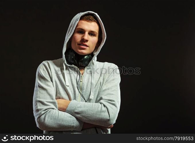 young serious hooded man teen boy with headphones listening to music black background