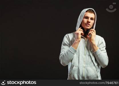 young serious hooded man teen boy with headphones listening to music black background