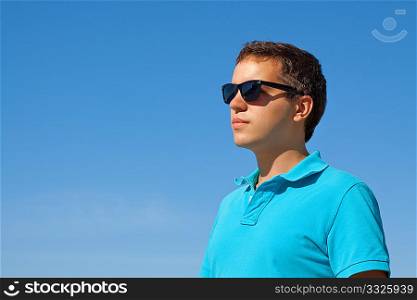 young serious man in sunglasses against blue sky