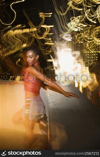 Young sexy African-American woman on patio in New York City, New York at night with blurred lights.