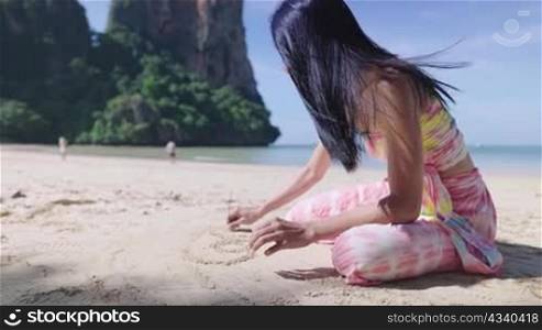 Young sexy beautiful asian lady sitdown playing with soft sand on the island beach, summer vacation travel booking resort reservation promotion, enjoy outdoor activity, sun bathing drawing on the sand