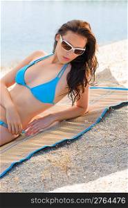 Young sexy bikini model lying on beach with sunglasses