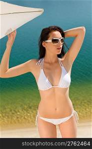 Young sexy bikini model posing with sunglasses by beach parasol