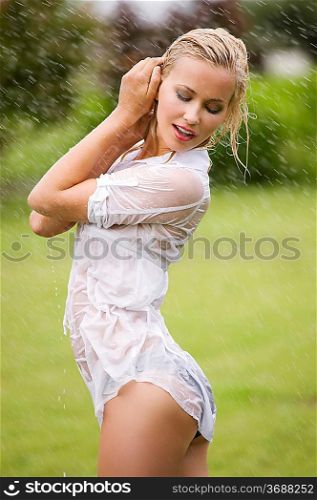 young sexy blond woman outdoor in a garden playing with splatter water with wet whit shirt