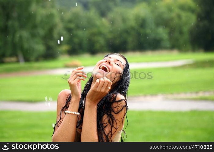 Young sexy brunette woman outdoor in a garden playing with water and rain with wet shirt