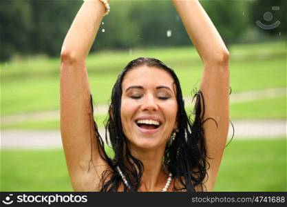 Young sexy brunette woman outdoor in a garden playing with water and rain with wet shirt