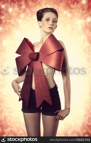 young sexy female posing in a creative christmas portrait with colorful make-up, big red bow on the breast, adorned like a sexy gift