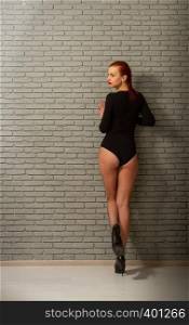young sexy girl with wet red hair in a black sports bodysuit and mesh pantyhose against a gray brick wall. girl grey wall