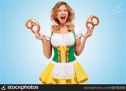 Young sexy indignant Oktoberfest woman wearing a traditional Bavarian dress dirndl holding two pretzels with an indignant mien on blue background.