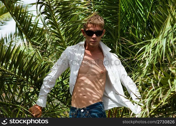 Young sexy man in sunglasses among palm trees on a windy day