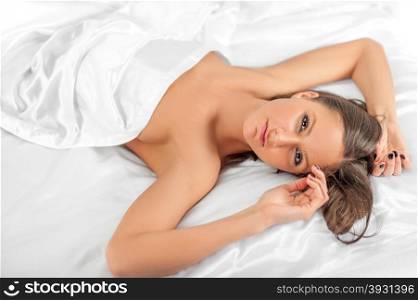 Young sexy nude woman lying under silk sheets