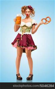 Young sexy Oktoberfest waitress wearing a traditional Bavarian dress dirndl holding a pretzel and beer mug, and making faces on blue background.