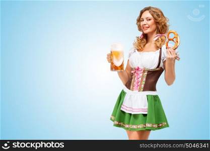 Young sexy Oktoberfest waitress wearing a traditional Bavarian dress dirndl offering a pretzel and beer mug on blue background.