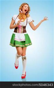 Young sexy Oktoberfest woman wearing a traditional Bavarian dress dirndl dancing with a pretzel in hands on blue background.