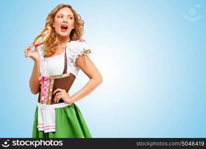 Young sexy Oktoberfest woman wearing a traditional Bavarian dress dirndl eating a pretzel on blue background.