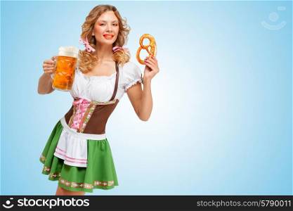 Young sexy Oktoberfest woman wearing a traditional Bavarian dress dirndl holding a pretzel and beer mug in hands on blue background.