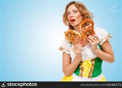 Young sexy Oktoberfest woman wearing a traditional Bavarian dress dirndl holding two pretzels and feeling scared on blue background.